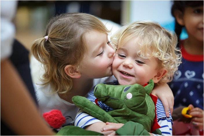 cute girl kissing young baby holding cuddly toy