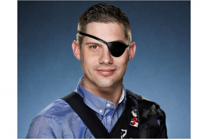 man with eye patch in studio headshot against blue backdrop